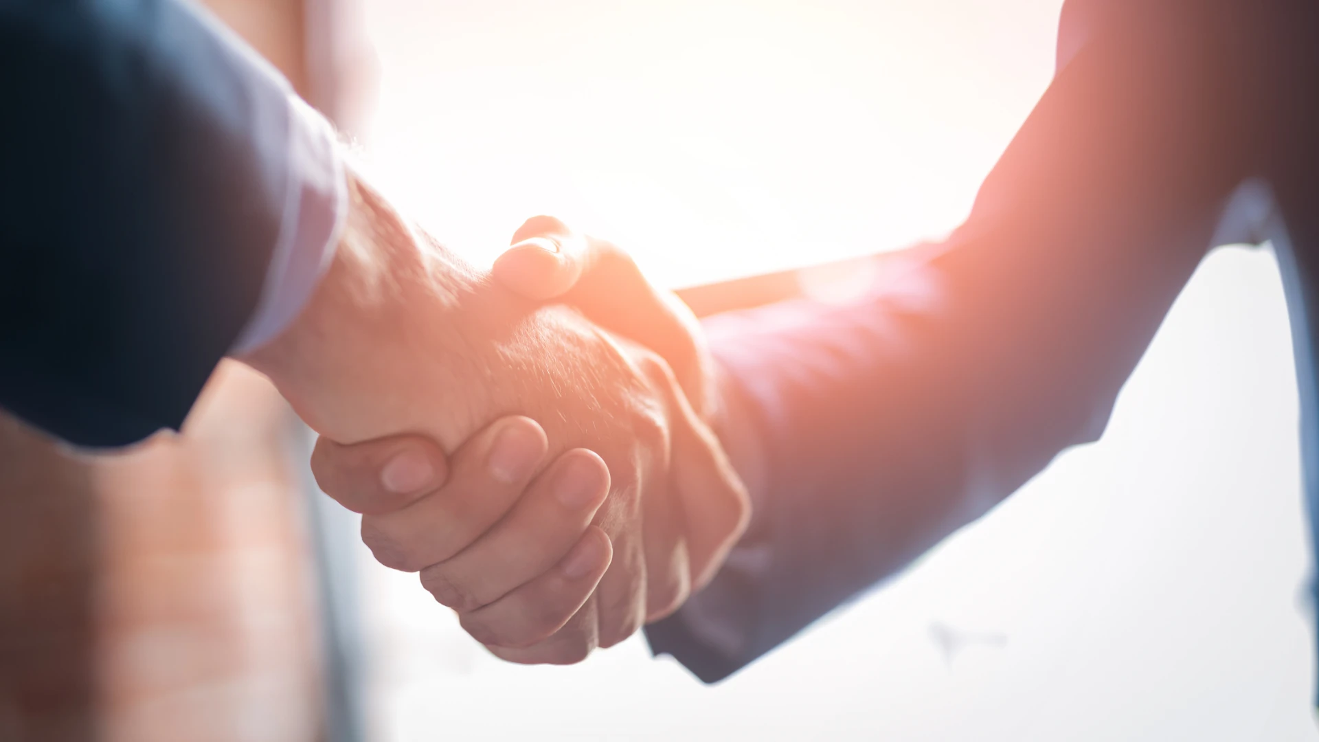 Two business professionals shaking hands in bright sunlight, symbolizing a trusted partnership